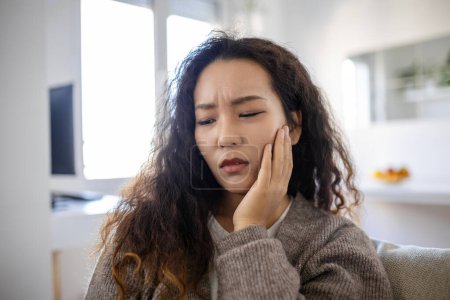 Téléchargez les photos : Portrait of unhappy young Asian woman suffering from toothache at home. Healthcare, dental health and problem concept. - en image libre de droit