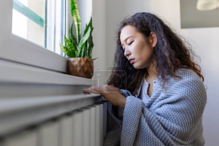 Foto de Asian Woman freezing at home, sitting by the cold radiator. Woman with home heating problem feeling cold - Imagen libre de derechos