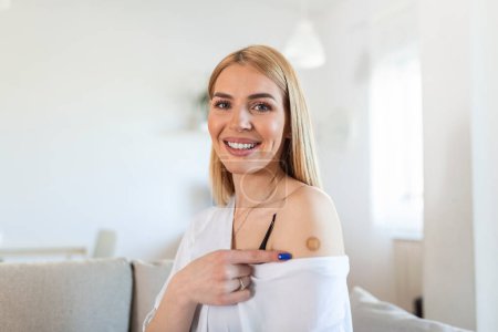 Photo for Woman pointing at his arm with a bandage after receiving the covid-19 vaccine. Young woman showing her shoulder after getting coronavirus vaccine - Royalty Free Image