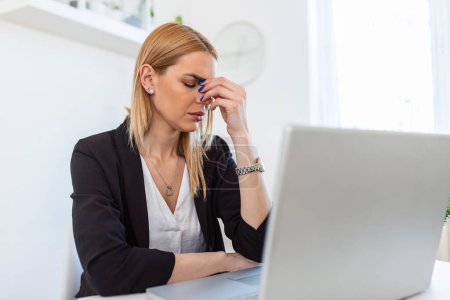 Foto de Feeling exhausted. Frustrated young woman looking exhausted while sitting at her working place and carrying her glasses in hand - Imagen libre de derechos