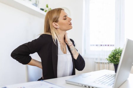 Foto de Retrato de una joven mujer estresada sentada en el escritorio de la oficina en casa delante de la computadora portátil, tocando el cuello dolorido con expresión dolorida, sufriendo de dolor de cuello después de trabajar en la PC - Imagen libre de derechos