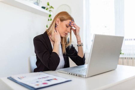 Photo for Young frustrated woman working at office desk in front of laptop suffering from chronic daily headaches, treatment online, appointing to a medical consultation, electromagnetic radiation, sick pay - Royalty Free Image