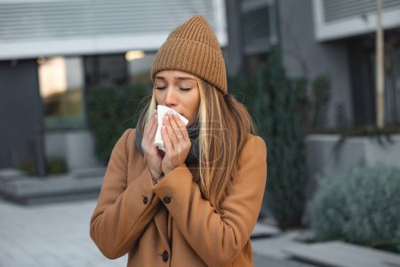 Photo for Ill beautiful young woman sneezing and blowing nose in napkin. Sick businesswoman in business style sneeze at street. Unhealthy employee. Outdoor. Virus symptoms. Cold disease. - Royalty Free Image