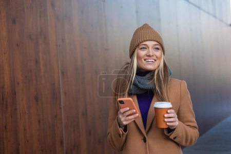 Téléchargez les photos : Belle femme va travailler avec café marchant près de l'immeuble de bureaux. Portrait de femme d'affaires réussie tenant tasse de boisson chaude. - en image libre de droit