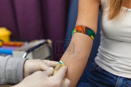 Photo for Preparation for blood test with pretty young woman by female doctor medical uniform on the table in white bright room. Nurse pierces the patient's arm vein with needle blank tube - Royalty Free Image