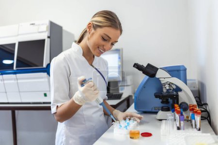 Foto de Closeup portrait, scientist pipetting from 50 mL conical tube with blue liquid solution, performing laboratory experiments, isolated lab . Forensics, genetics, microbiology, biochemistry - Imagen libre de derechos