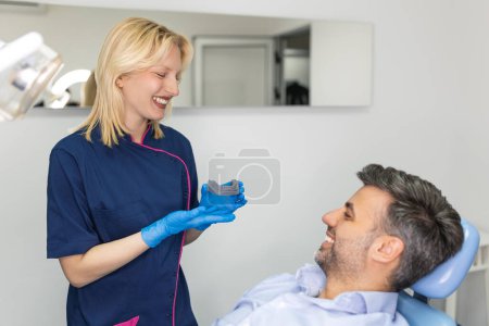 Téléchargez les photos : Jolie dentiste médecin femme montrant modèle de mâchoire à la clinique dentaire, concept de soins dentaires. Concept de soins dentaires. Jeune femme dentiste montrant un modèle de mâchoire de patient masculin à la clinique dentaire - en image libre de droit