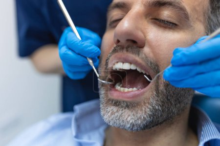 Foto de Dentista examinando los dientes de un paciente en el consultorio del dentista. Paciente masculino que recibe tratamiento dental en el consultorio del dentista - Imagen libre de derechos