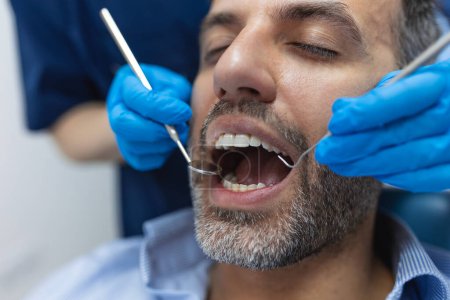 Foto de Imagen del paciente varón satisfecho sentado en la silla dental en el centro médico mientras que el médico profesional que fija sus dientes - Imagen libre de derechos