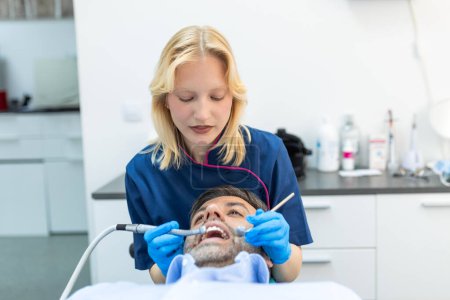 Téléchargez les photos : Dentiste et patient au centre médical. Le docteur traite les dents d'un homme avec une perceuse dentaire. Orthodontiste et prothésiste. Hygiène et dents saines. - en image libre de droit