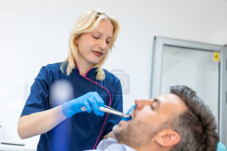 Photo for Treatment of a patient with a dentist surgeon. Extraction of teeth and prosthetics. Doctor performing extraction procedure with forceps removing patient tooth. Healthcare dentistry medicine concept - Royalty Free Image