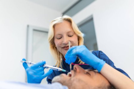 Photo for Painkiller anesthesia injection. Dentist examining a patient's teeth in modern dentistry office. Closeup cropped picture with copyspace. Female Doctor in blue uniform. - Royalty Free Image