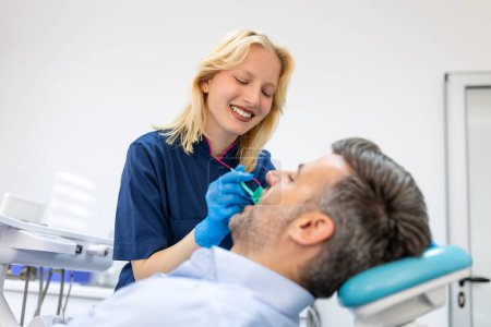 Photo for Female dentist treating teeth to patient, mid age man in chair at dental clinic. Dentistry, healthy teeth, medicine and healthcare concept - Royalty Free Image