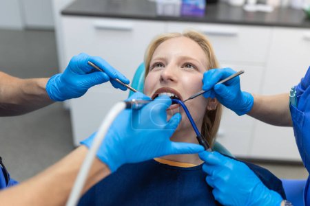 Téléchargez les photos : Gros plan d'une procédure de forage dentaire chez un dentiste s'approchant d'un patient avec des instruments dentaires tenus dans les mains protégés par des gants chirurgicaux - en image libre de droit