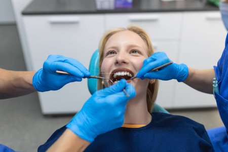 Téléchargez les photos : Gros plan d'une procédure de forage dentaire chez un dentiste s'approchant d'un patient avec des instruments dentaires tenus dans les mains protégés par des gants chirurgicaux - en image libre de droit