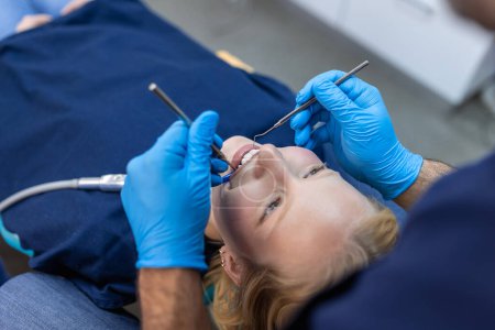 Téléchargez les photos : Over the shoulder view of a dentist examining a patients teeth in dental clinic. Female having her teeth examined by a dentist. - en image libre de droit