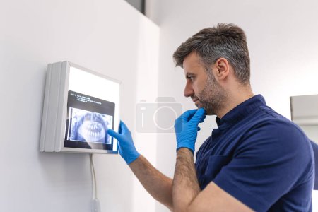 Foto de Profesional dental de la salud en uniformes azules que examinan la radiografía dental en la pantalla de la computadora. Dentistas que buscan rayos X en monitor en clínica dental. - Imagen libre de derechos