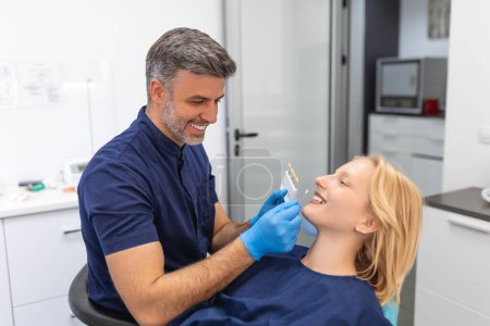 Foto de Patient's teeth shade with samples for bleaching treatment.Viewed oral hygiene. Woman at the dentist. Woman in the dental chair dental treatment during surgery. - Imagen libre de derechos