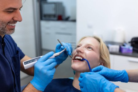 Photo for Image of satisfied young woman sitting in dental chair at medical center while professional doctor fixing her teeth - Royalty Free Image