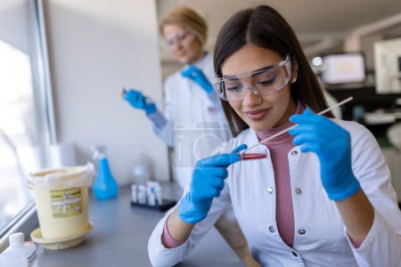Foto de Placa de Petri en la mano de un joven científico cerca del microscopio en laboratorio. Examen de placa de cultivo bacteriano por una investigadora femenina en laboratorio de microbiología - Imagen libre de derechos