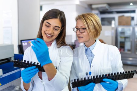 Photo for Two scientists are working in laboratory. Young female researcher and her senior supervisor are doing investigations with test tubes. - Royalty Free Image