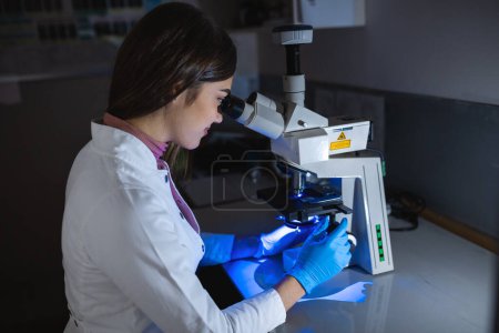 Téléchargez les photos : Scientifique à la recherche d'un plat de Petri avec des produits chimiques d'échantillon génétiquement modifiés sous un microscope. Microbiologiste travaillant dans un laboratoire moderne avec des équipements technologiques. - en image libre de droit
