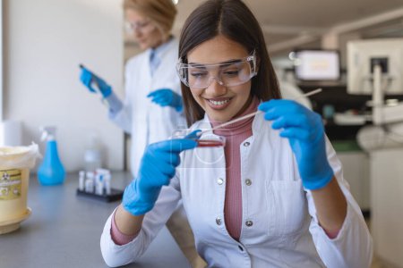 Foto de Placa de Petri en la mano de un joven científico cerca del microscopio en laboratorio. Examen de placa de cultivo bacteriano por una investigadora femenina en laboratorio de microbiología - Imagen libre de derechos