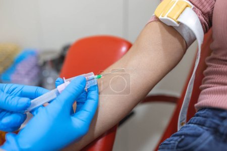 Photo for Preparation for blood test with pretty young woman by female doctor medical uniform on the table in white bright room. Nurse pierces the patient's arm vein with needle blank tube - Royalty Free Image