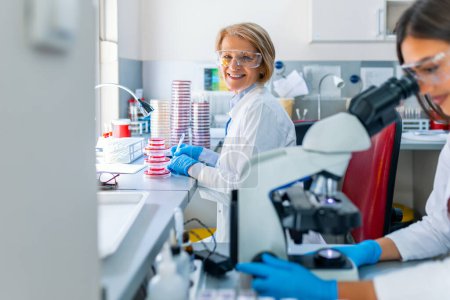 Photo for Young scientists conducting research investigations in a medical laboratory, a researcher in the foreground is using a microscope - Royalty Free Image