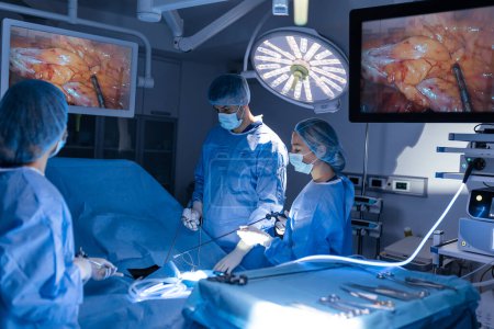 Foto de Tres cirujanos haciendo cirugía laparoscópica. Médicos mirando la imagen en el monitor. Concepto de medicina y salud. Órgano interno del paciente visto en el monitor del ordenador - Imagen libre de derechos