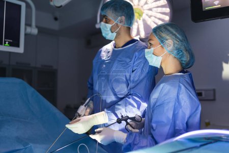 Foto de Vista posterior del equipo de cirujanos observa los monitores mientras se realiza la operación de preformación en el quirófano del hospital, paciente operado por cirujano masculino que trabaja con instrumentos de laparoscopia quirúrgica. - Imagen libre de derechos