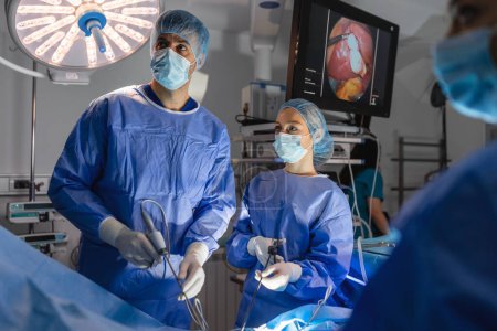 Foto de Tres cirujanos haciendo cirugía laparoscópica. Médicos mirando la imagen en el monitor. Concepto de medicina y salud. Órgano interno del paciente visto en el monitor del ordenador - Imagen libre de derechos
