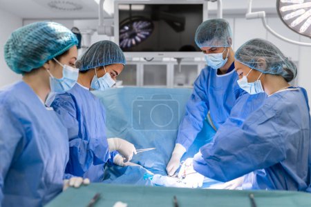 Foto de Equipo quirúrgico que realiza cirugía en quirófano moderno, Equipo de médicos que se concentran en un paciente durante una cirugía, Equipo de médicos que trabajan juntos durante una cirugía en quirófano
, - Imagen libre de derechos