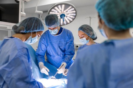Foto de Medical team performing operation. Group of surgeon at work in operating theatre toned in blue. Doctor operation in operation room at hospital concept for insurance advertising. - Imagen libre de derechos
