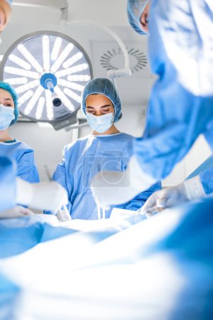 Photo for Preparation for the beginning of surgical operation with a cut. Group of surgeons at work in operating theater toned in blue. Medical team performing operation - Royalty Free Image