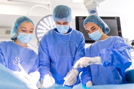 Photo for Group of medical team urgently doing surgical operation and helping patient in theater at hospital. Medical team performing surgical operation in a bright modern operating room - Royalty Free Image