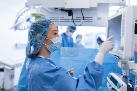 Téléchargez les photos : Portrait d'une jeune femme médecin en gommage et masque protecteur préparant une machine d'anesthésie avant une opération - en image libre de droit