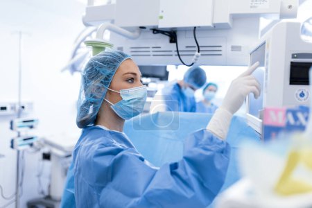 Téléchargez les photos : Portrait d'une jeune femme médecin en gommage et masque protecteur préparant une machine d'anesthésie avant une opération - en image libre de droit