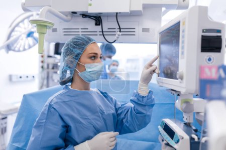 Photo for Anesthesiologist keeping track of vital functions of the body during cardiac surgery. Surgeon looking at medical monitor during surgery. Doctor checking monitor for patient health status. - Royalty Free Image