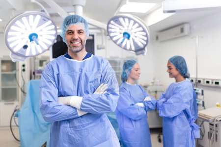 Photo for Portrait of male surgeon standing with arms crossed in operation theater at hospital. Team surgeons are performing an operation, middle aged doctor is looking at camera, in a modern operating room - Royalty Free Image