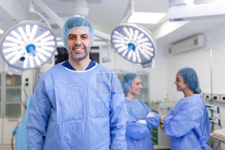 Téléchargez les photos : Portrait d'un chirurgien homme debout les bras croisés en salle d'opération à l'hôpital. Les chirurgiens d'équipe effectuent une opération, médecin d'âge moyen regarde la caméra, dans une salle d'opération moderne - en image libre de droit