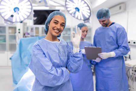 Foto de Portrait of female woman nurse surgeon OR staff member dressed in surgical scrubs gown mask and hair net in hospital operating room theater making eye contact smiling pleased happy looking at camera - Imagen libre de derechos