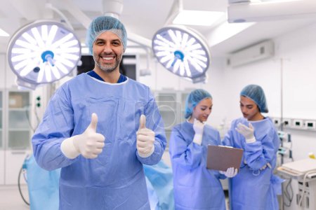 Photo for Portrait of male surgeon standing with arms crossed in operation theater at hospital. Team surgeons are performing an operation, middle aged doctor is looking at camera, in a modern operating room - Royalty Free Image