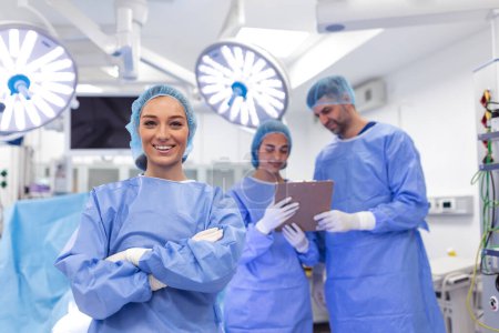 Téléchargez les photos : Portrait of female woman nurse surgeon OR staff member dressed in surgical scrubs gown mask and hair net in hospital operating room theater making eye contact smiling pleased happy looking at camera - en image libre de droit