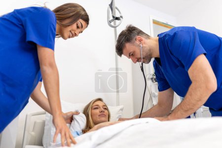 Téléchargez les photos : Hôpital Ward : Amical médecin et infirmière prenant soin de belle patiente caucasienne se reposant au lit. Le médecin explique les résultats des tests. Femme se rétablissant après une chirurgie réussie - en image libre de droit