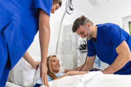 Téléchargez les photos : Hospital Ward Friendly Médecin et infirmière prenant soin de belle patiente caucasienne se reposant au lit. Le médecin explique les résultats des tests. Femme se rétablissant après une chirurgie réussie - en image libre de droit