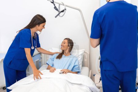 Téléchargez les photos : Femme hospitalisée allongée au lit pendant que le médecin la surveille. Médecin et infirmière examinant une patiente dans une chambre d'hôpital. - en image libre de droit