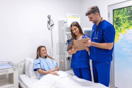 Photo for Doctors in uniform with stethoscope using clipboard standing in hospital ward with patient resting in bed on background. Practitioner checking patient data - Royalty Free Image
