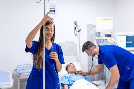 Photo for Young woman doctor anesthesiologist dressed in blue gown, puts the IV dropper in hospital room - Royalty Free Image