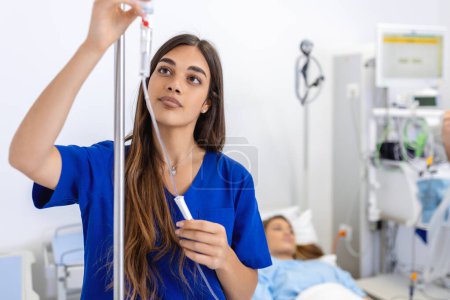 Téléchargez les photos : Jeune femme médecin anesthésiste vêtue de robe bleue, met le compte-gouttes IV dans la chambre d'hôpital - en image libre de droit